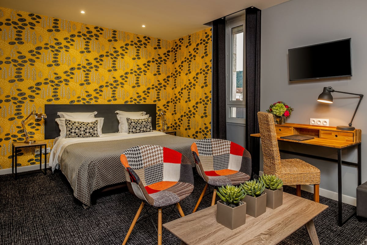 Habitación de hotel con cama, dos sillones, escritorio con computadora, televisor y ventana.