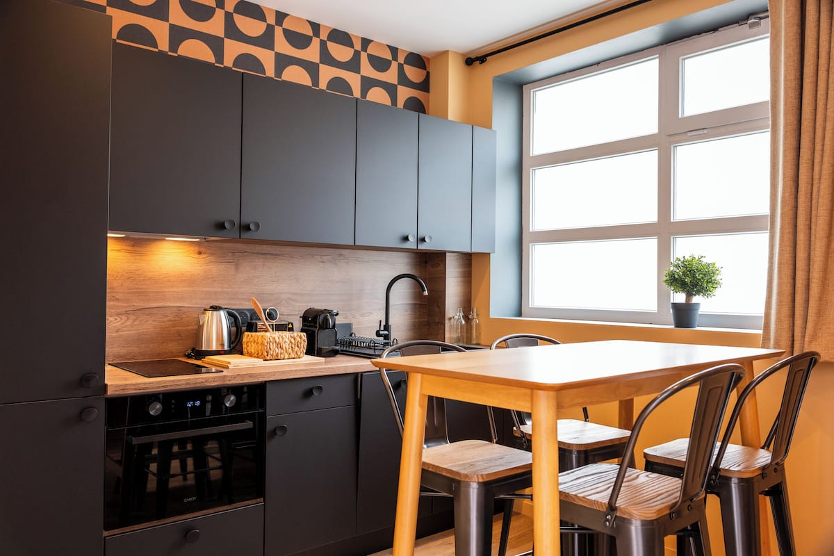 Una cocina moderna con armarios oscuros, encimera de madera, una estufa y una ventana con una planta.