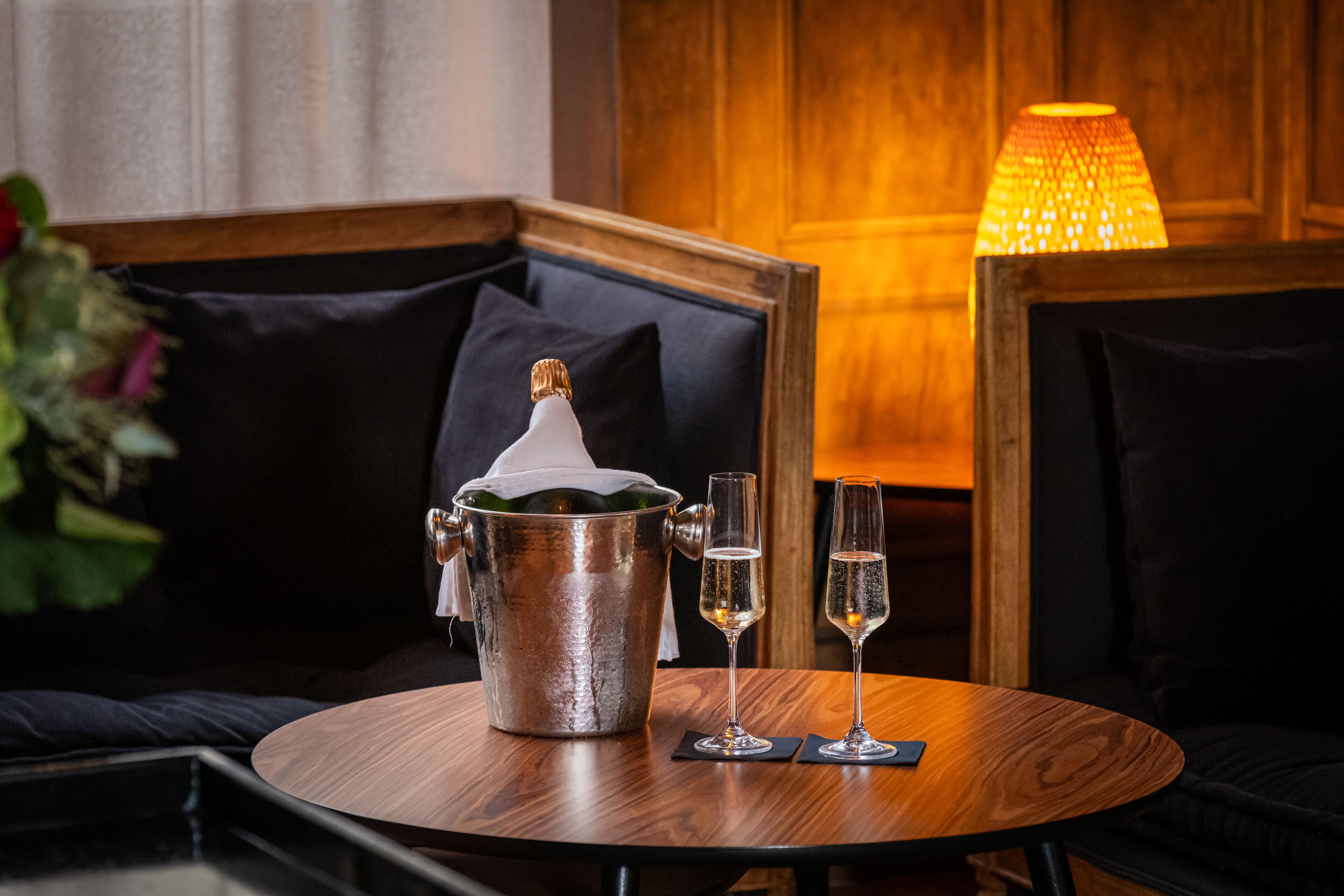 A cozy room with a wooden table, a metal bucket with a bottle, and two glasses of champagne.