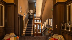 A hallway with a carpeted staircase, framed pictures on the walls, and a small table with flowers. - Nouvel Hôtel & Appartements (Oyonnax)