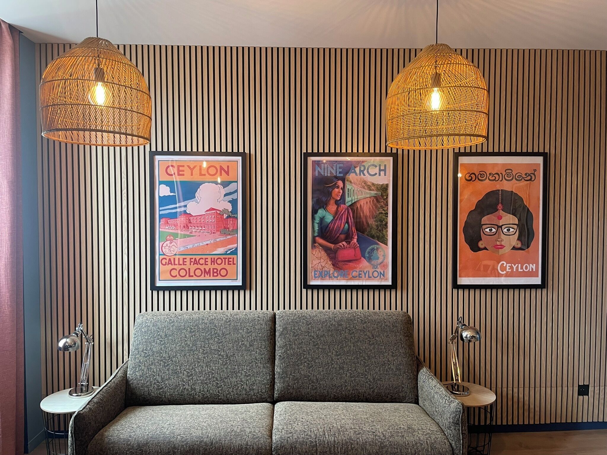 A modern room with a grey sofa, two hanging wicker lamps, and three framed posters on the wall.