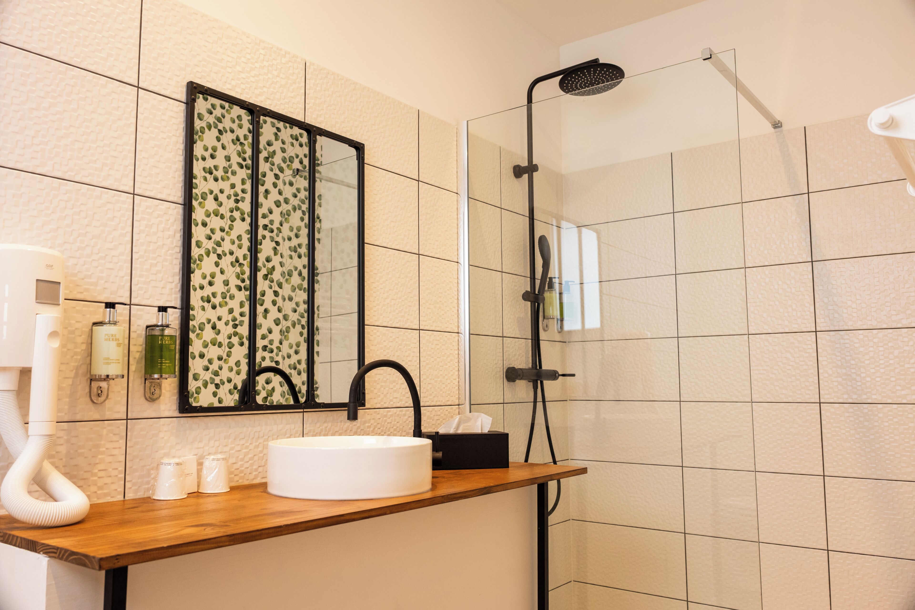 A bathroom with a wooden vanity, a white sink, a mirror with a leaf pattern, and a shower with a handheld showerhead.