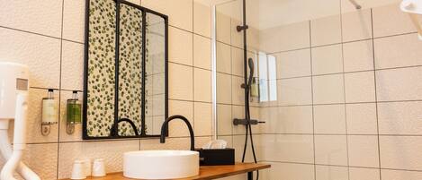 A bathroom with a wooden vanity, a white sink, a mirror with a leaf pattern, and a shower with a handheld showerhead.