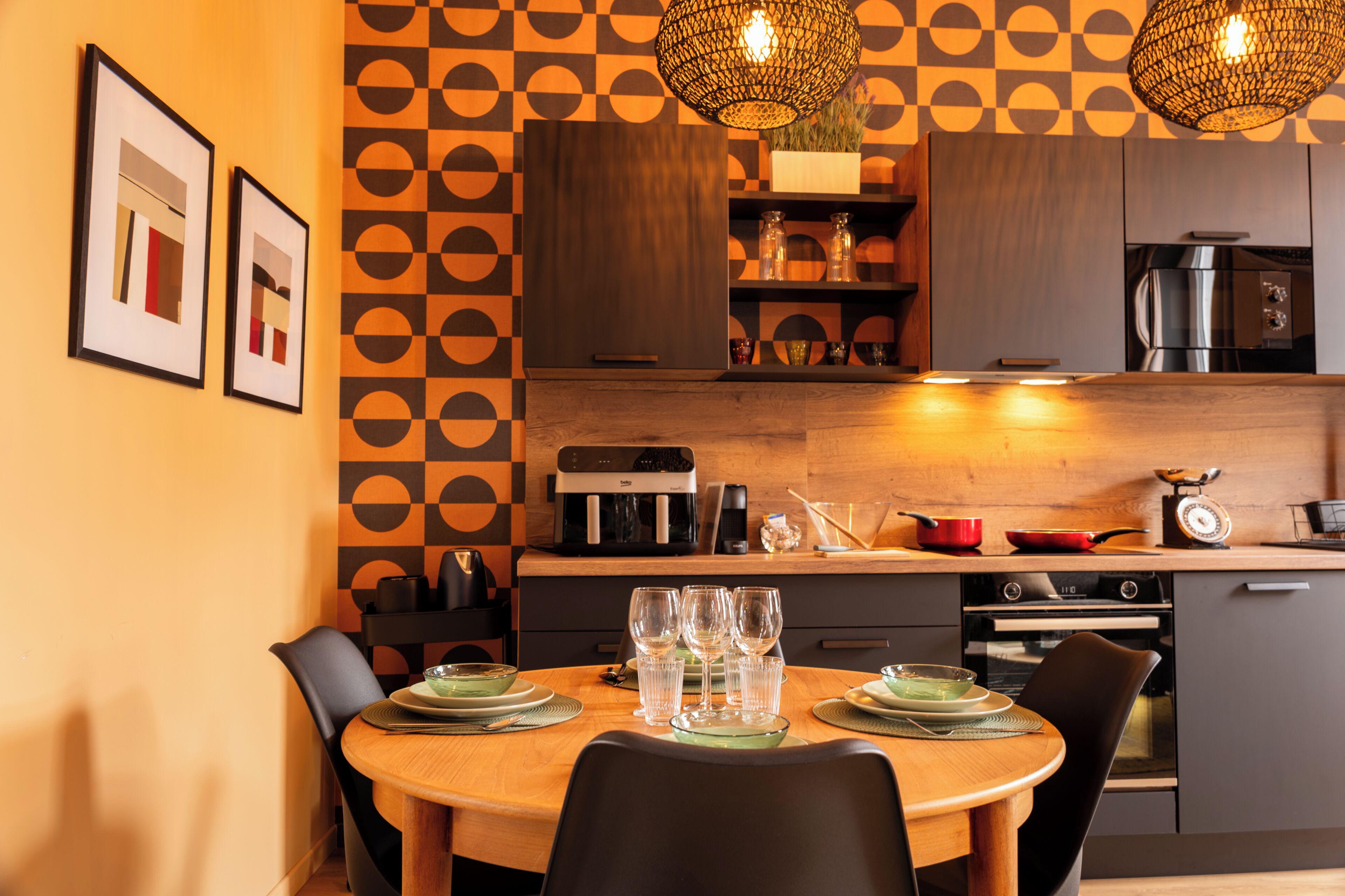 Uma cozinha moderna com área de refeições, destacando uma parede estampada, armários de madeira e uma mesa redonda com cadeiras.
