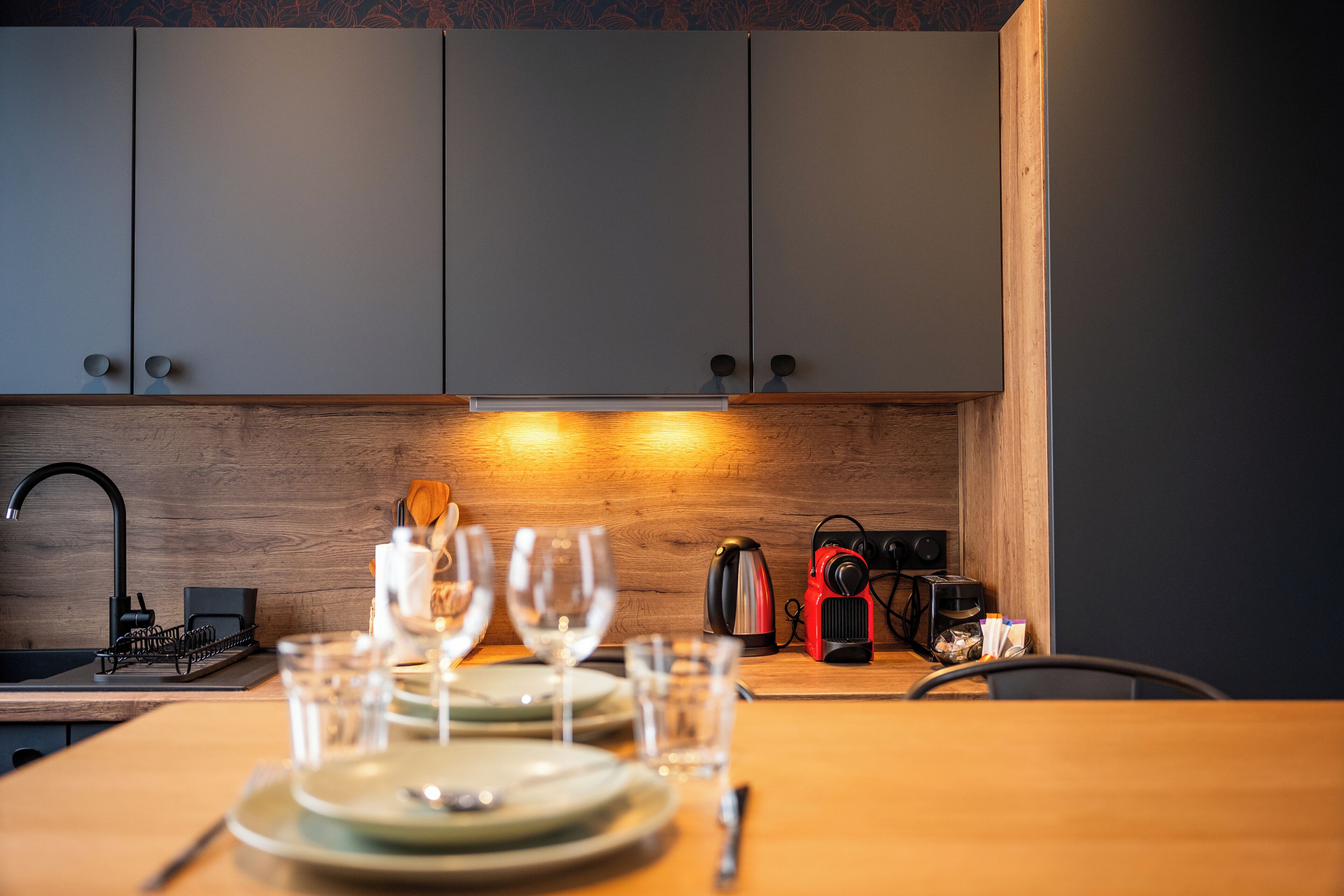 Una cocina moderna con armarios grises, encimera de madera, hervidor y cafetera.