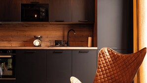 Una cocina moderna con armarios oscuros, encimera de madera, tetera, fregadero y una silla original.