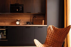 Una cocina moderna con armarios oscuros, encimera de madera, tetera, fregadero y una silla original.
