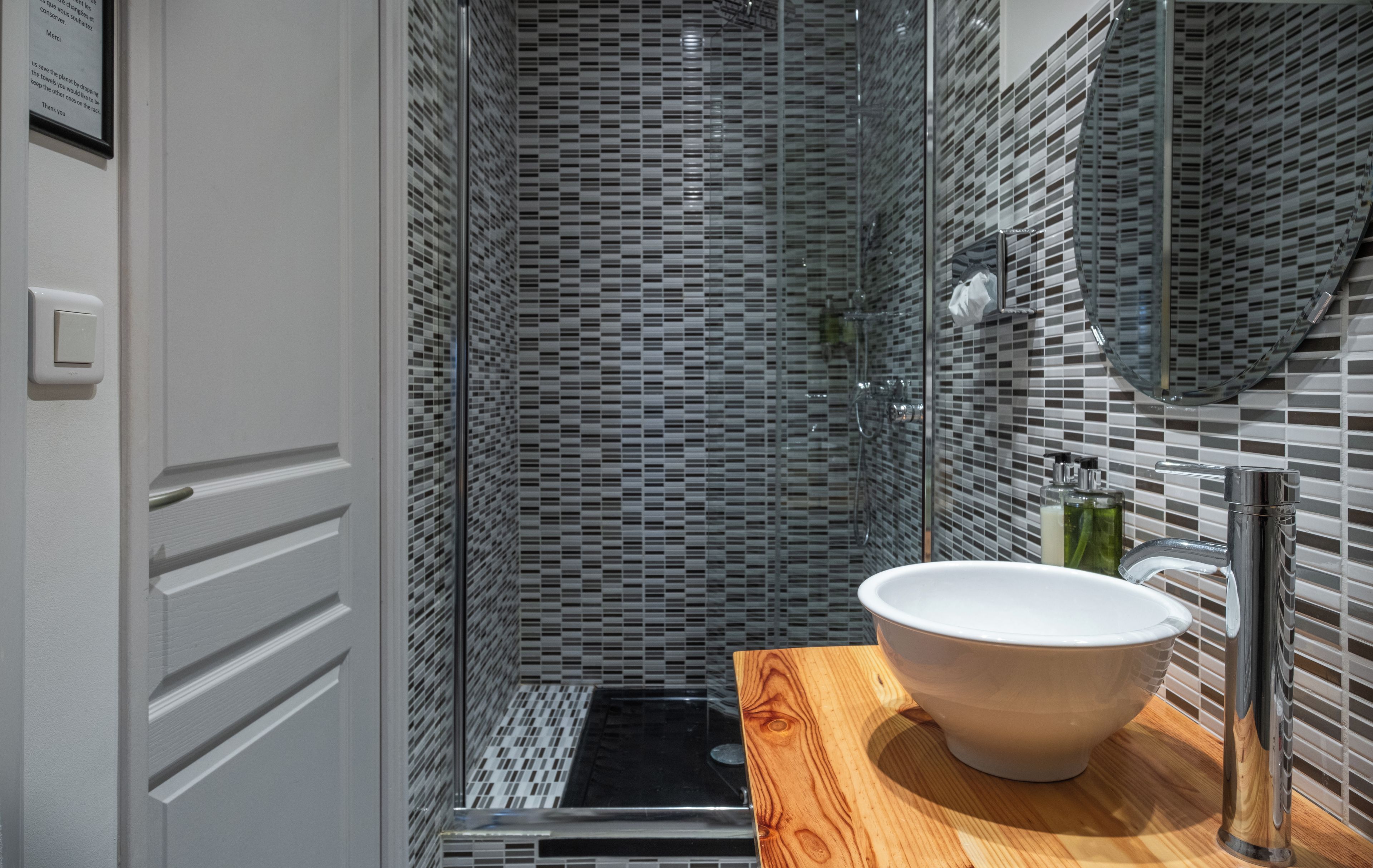 Un baño con lavamanos blanco, encimera de madera y cabina de ducha con mampara de vidrio y pared revestida de azulejos.