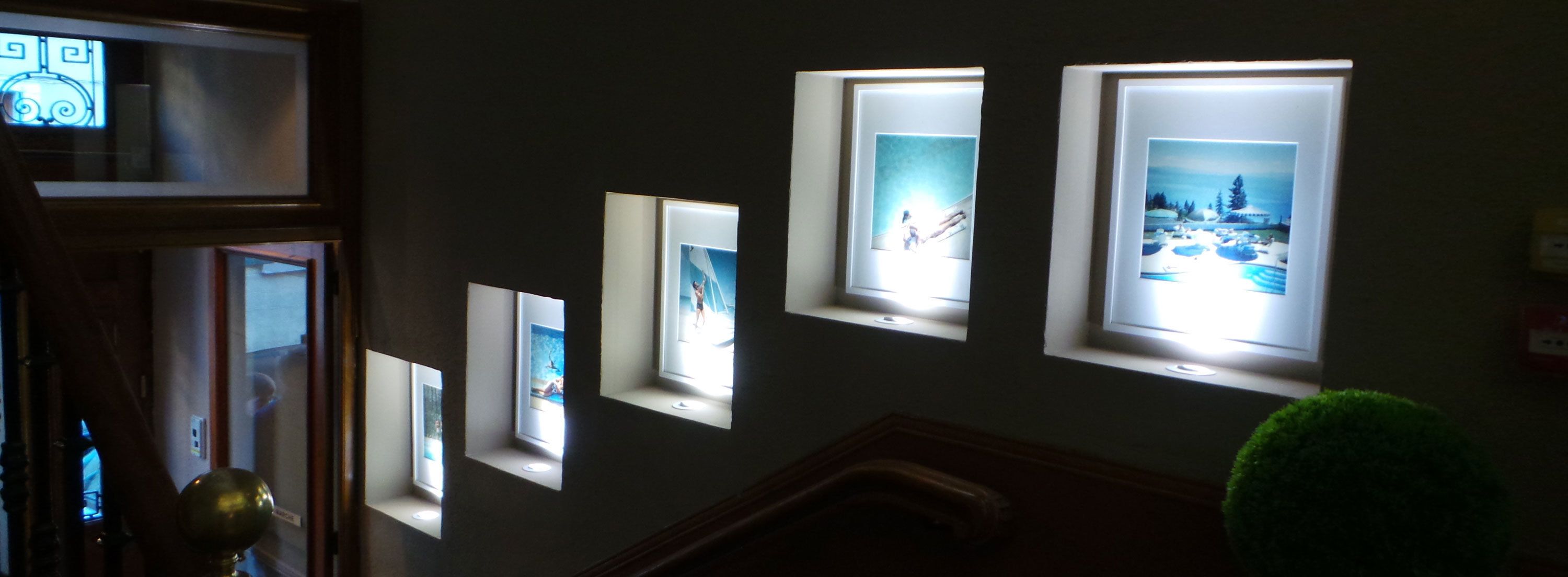 A hallway with multiple framed pictures illuminated by natural light from windows.
