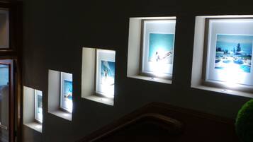 A hallway with multiple framed pictures illuminated by natural light from windows.