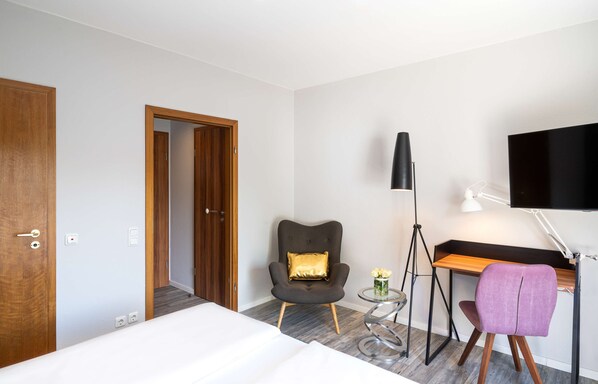 A hotel room with a bed, a desk, a chair, a lamp, and a TV. - Arthotel ANA GOLD (Augsburg)