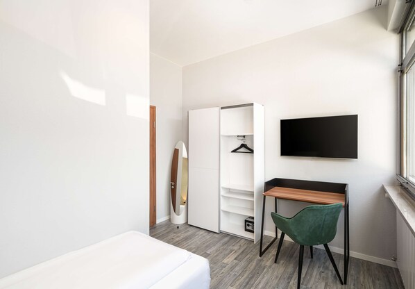 A modern bedroom with a bed, a desk, a chair, a wardrobe, and a TV. - Arthotel ANA GOLD (Augsburg)