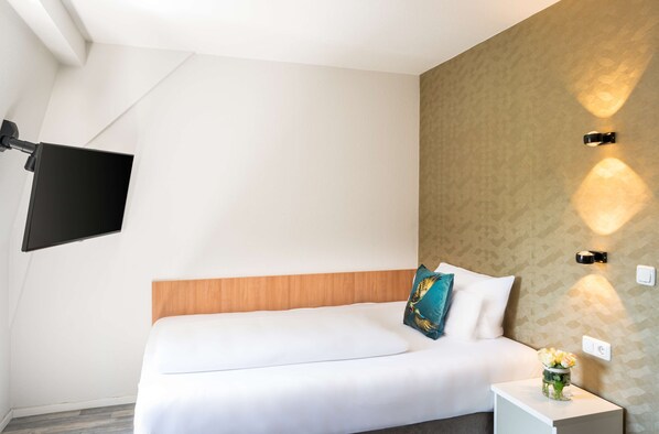 A modern hotel room with a bed, a nightstand with a vase of flowers, a mounted TV, and wall-mounted lighting. - Arthotel ANA GOLD (Augsburg)