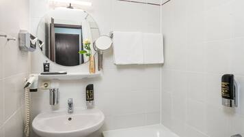 Un baño moderno con un lavamanos blanco, un espejo redondo, un espejo de mano, un perchero para toallas, un dispensador de jabón y un secamanos automático.