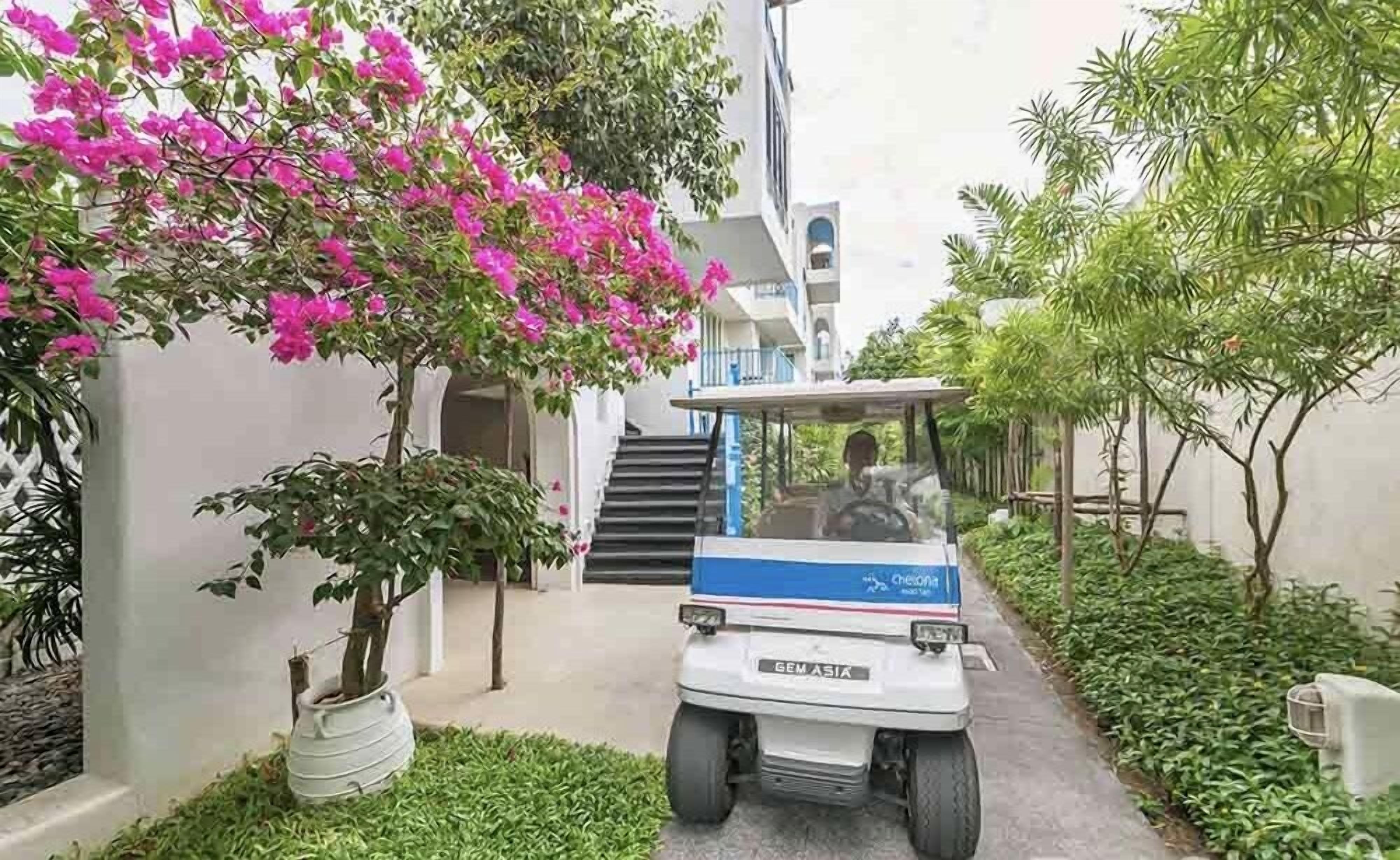 A white golf cart with "GEM ASIA" branding parked in a narrow alleyway with a staircase leading to a building.