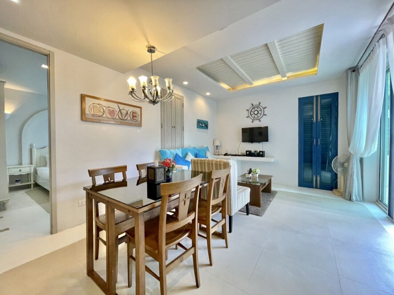 A modern living room with a dining area, a TV mounted on the wall, and a large window with curtains.