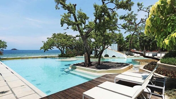 A poolside area with lounge chairs, a tree, and a view of the ocean. - Chelona Huahin Condo Garden View by Dome (Hua Hin)