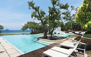 A poolside area with lounge chairs, a tree, and a view of the ocean. - Chelona Huahin Condo Garden View by Dome (Hua Hin)