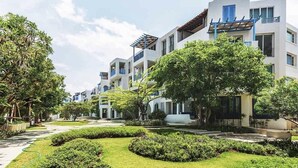 A modern residential building with multiple balconies, surrounded by well-maintained gardens and trees. - Chelona Huahin Condo Garden View by Dome (Hua Hin)