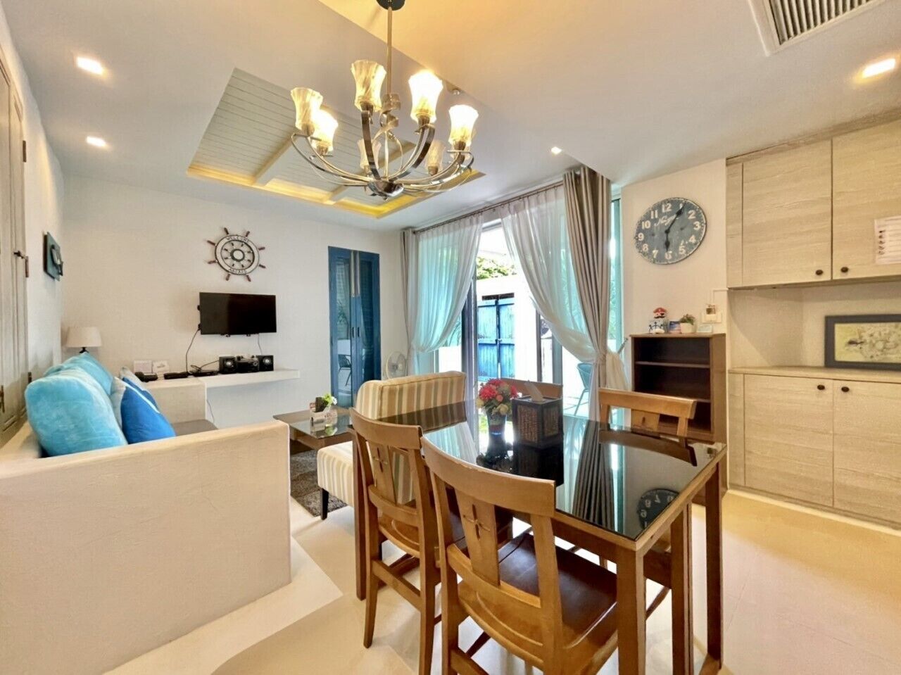 A modern living room with a dining area, a flat-screen TV, a clock, and a ceiling fan.