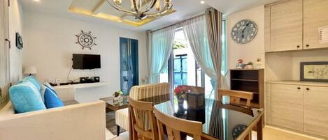 A modern living room with a dining area, a flat-screen TV, a clock, and a ceiling fan.