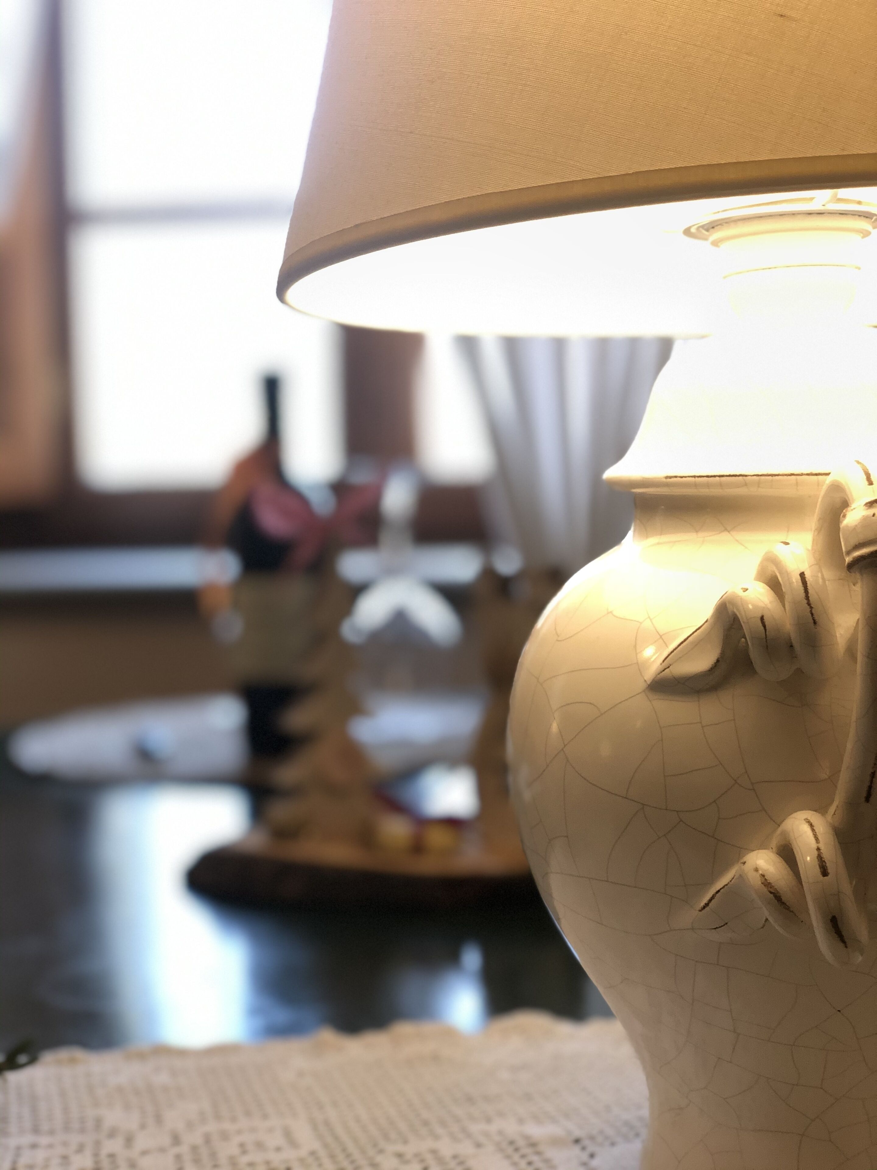 Un primo piano di una lampada in ceramica bianca dalla superficie strutturata, posata su un tavolo con un sottotavolo all'uncinetto.