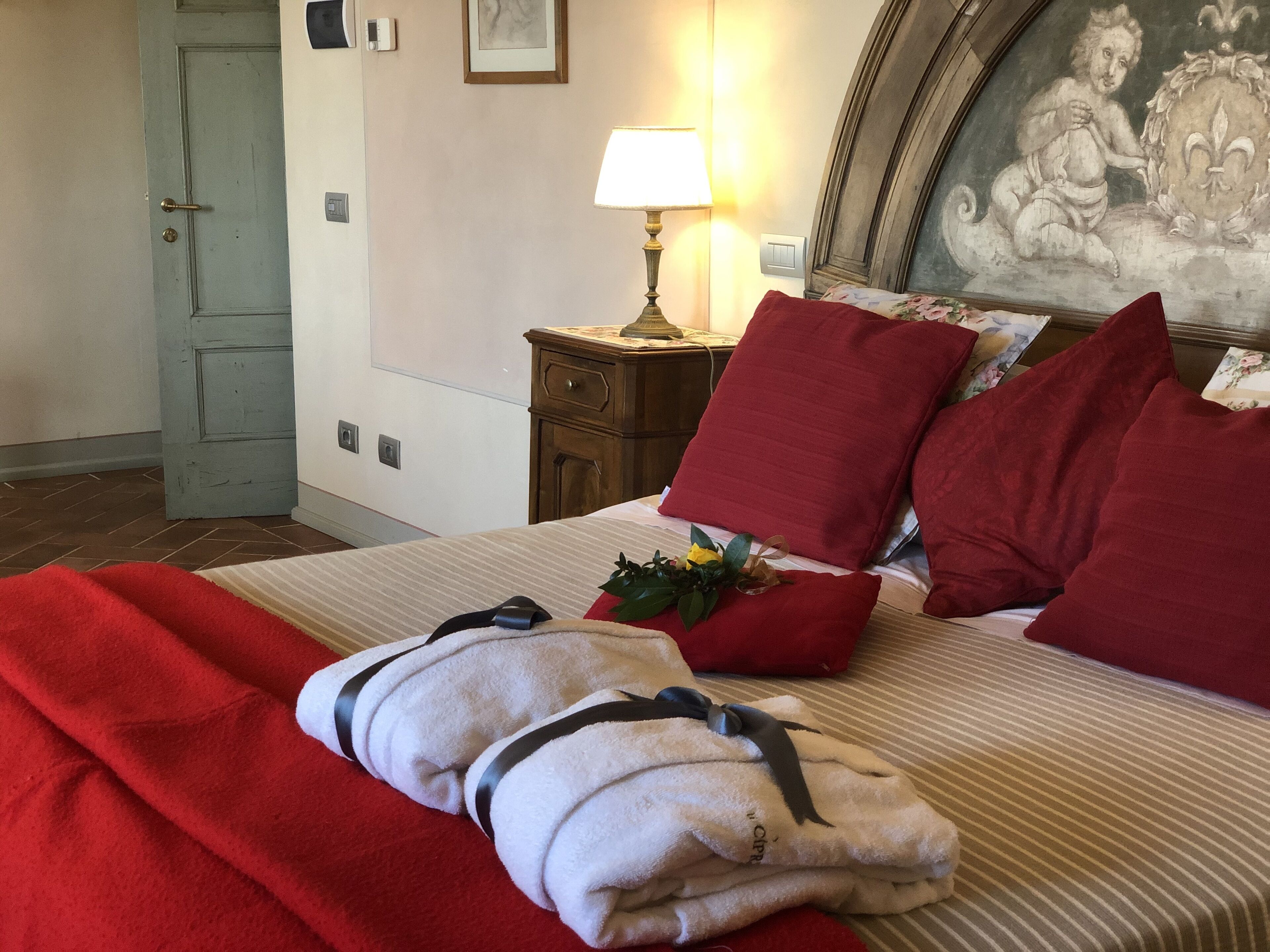 Une chambre d’hôtel avec un lit, des oreillers rouges, une lampe, un tableau au mur et une porte.