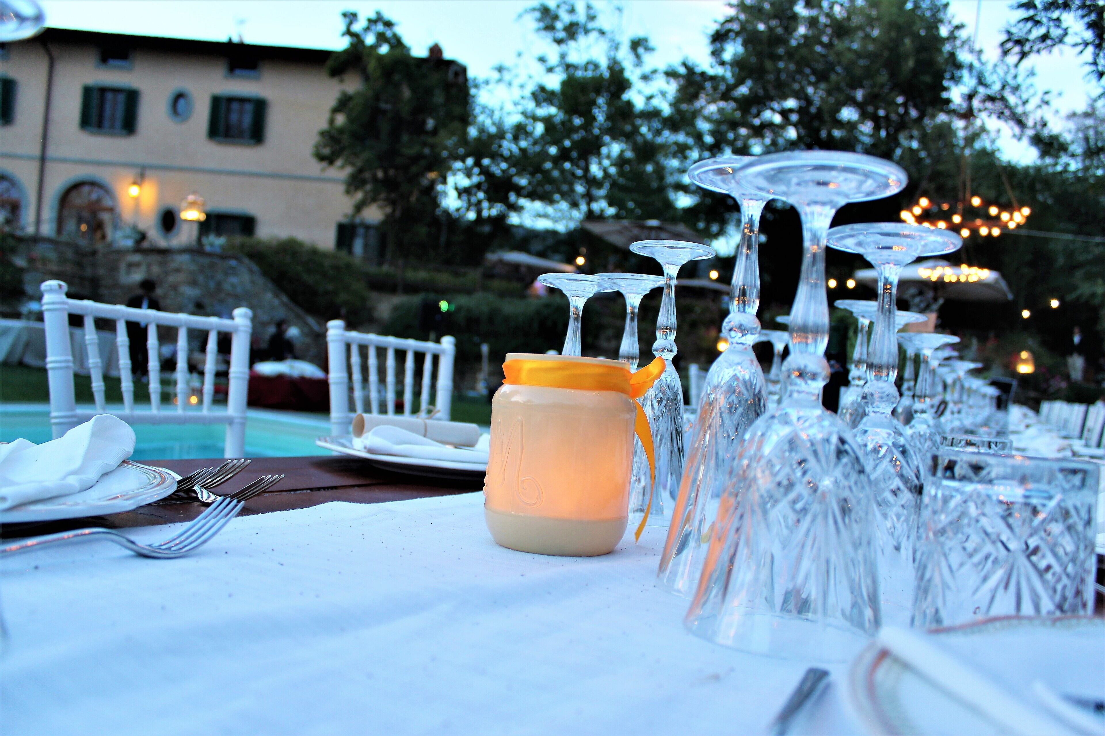 A dining table set with clear glassware, a jar with a yellow lid, and a white tablecloth.