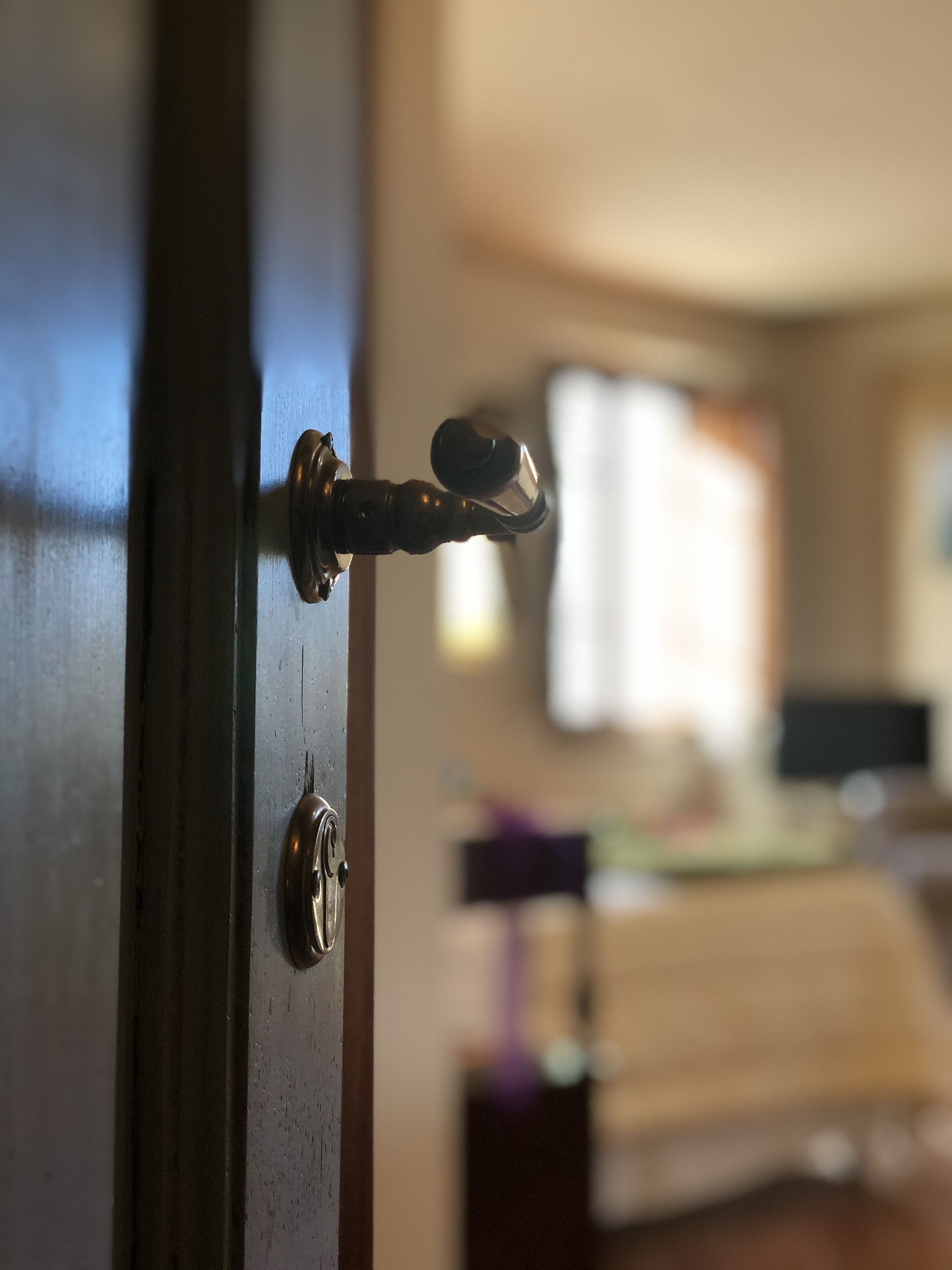 A close-up of a door lock with a keyhole, a window with blinds, and a blurred interior background.