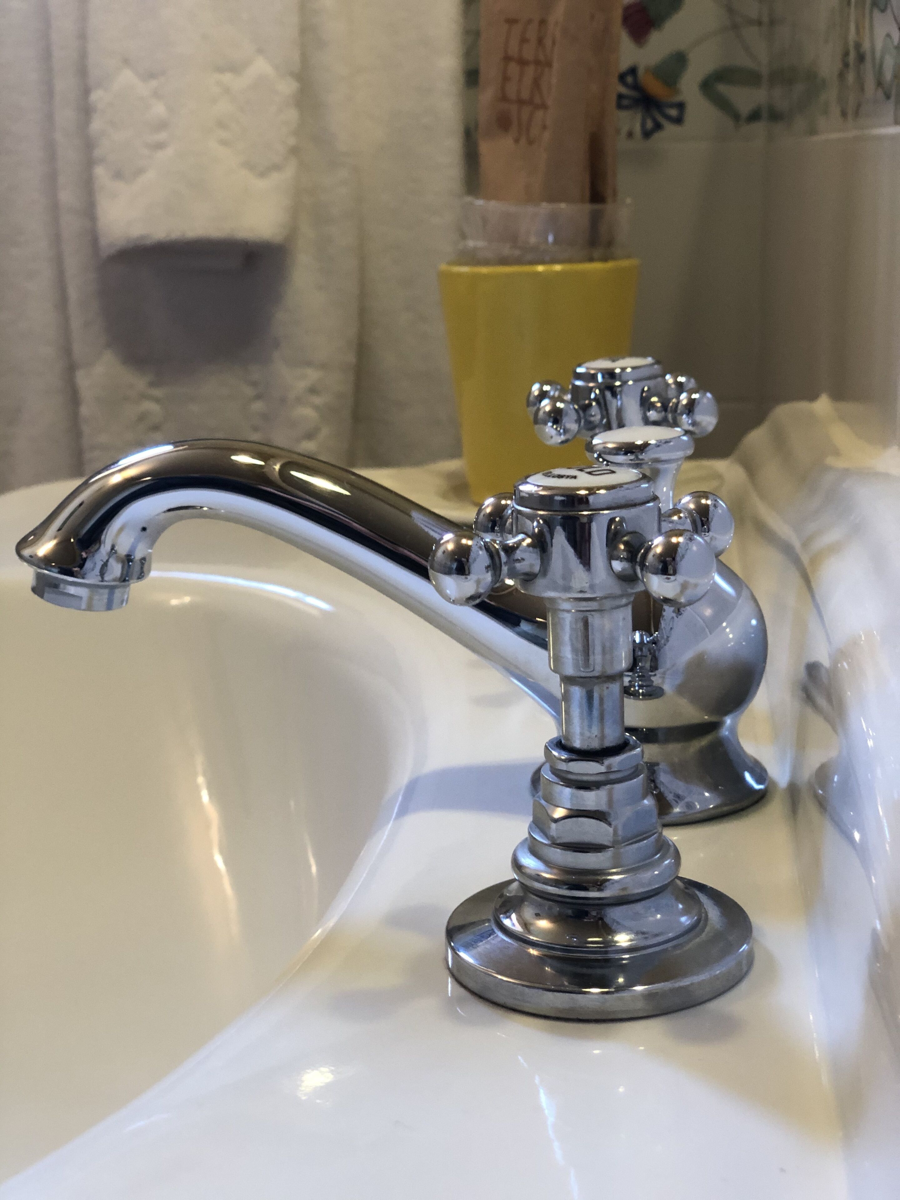 A bathroom sink with a chrome faucet and a glass of yellow liquid.