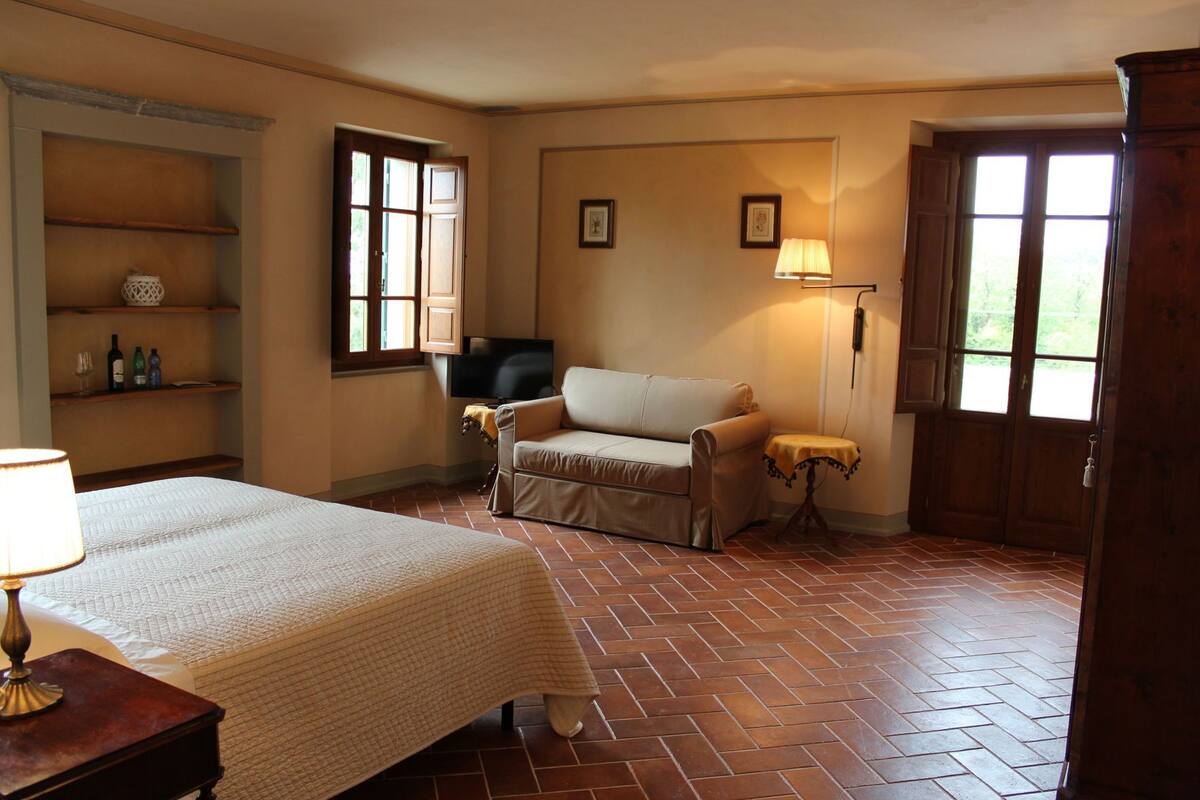 A room with a bed, a sofa, a television, a lamp, and a door.
