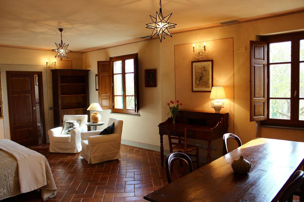A room with a bed, a dining table, a chair, a lamp, and a star-shaped ceiling light.