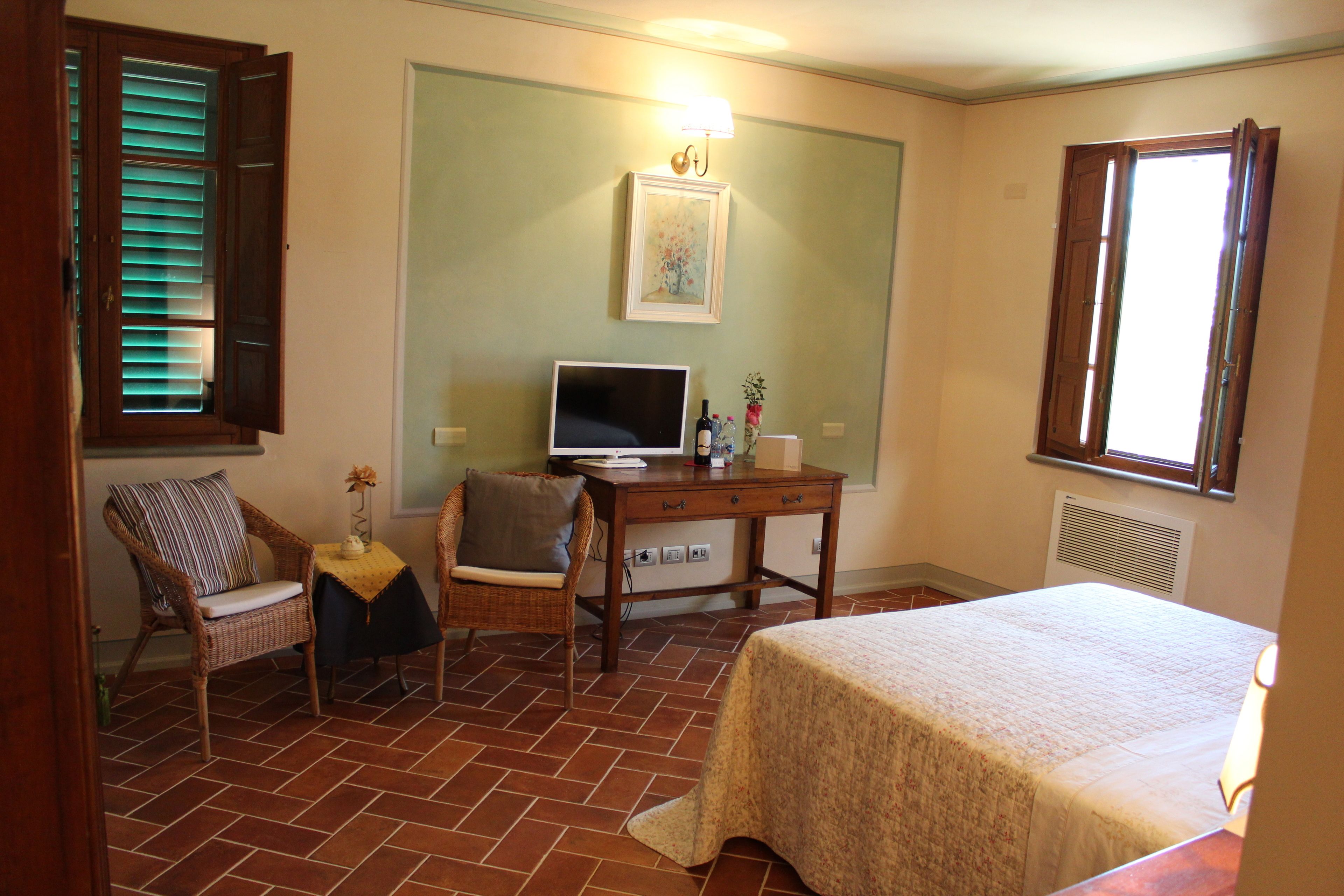Une chambre à coucher avec un lit, un bureau avec un ordinateur, une chaise et une fenêtre.