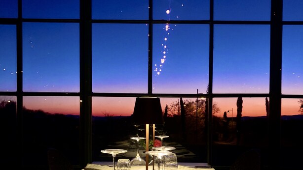 A dining table set for two with a view of the night sky through large windows. - La Cantina Relais - Fattoria Il Cipresso (Arezzo)