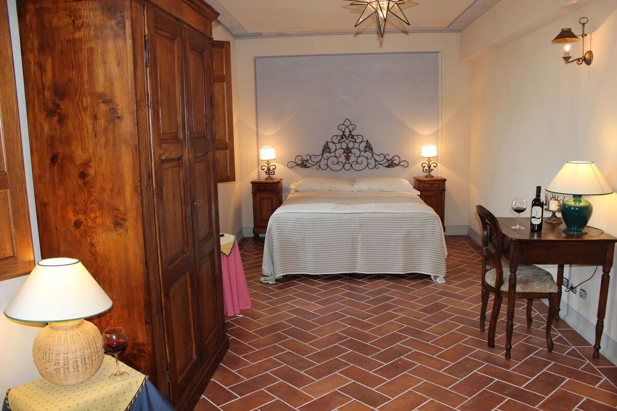 Un dormitorio con una cama, dos mesitas de noche, una silla, una mesa, una lámpara y un adorno en la pared.