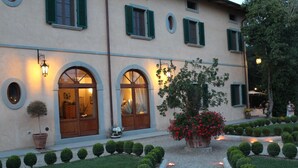 A building with arched windows and a well-maintained garden with trimmed bushes and a large flower pot. - La Cantina Relais - Fattoria Il Cipresso (Arezzo)