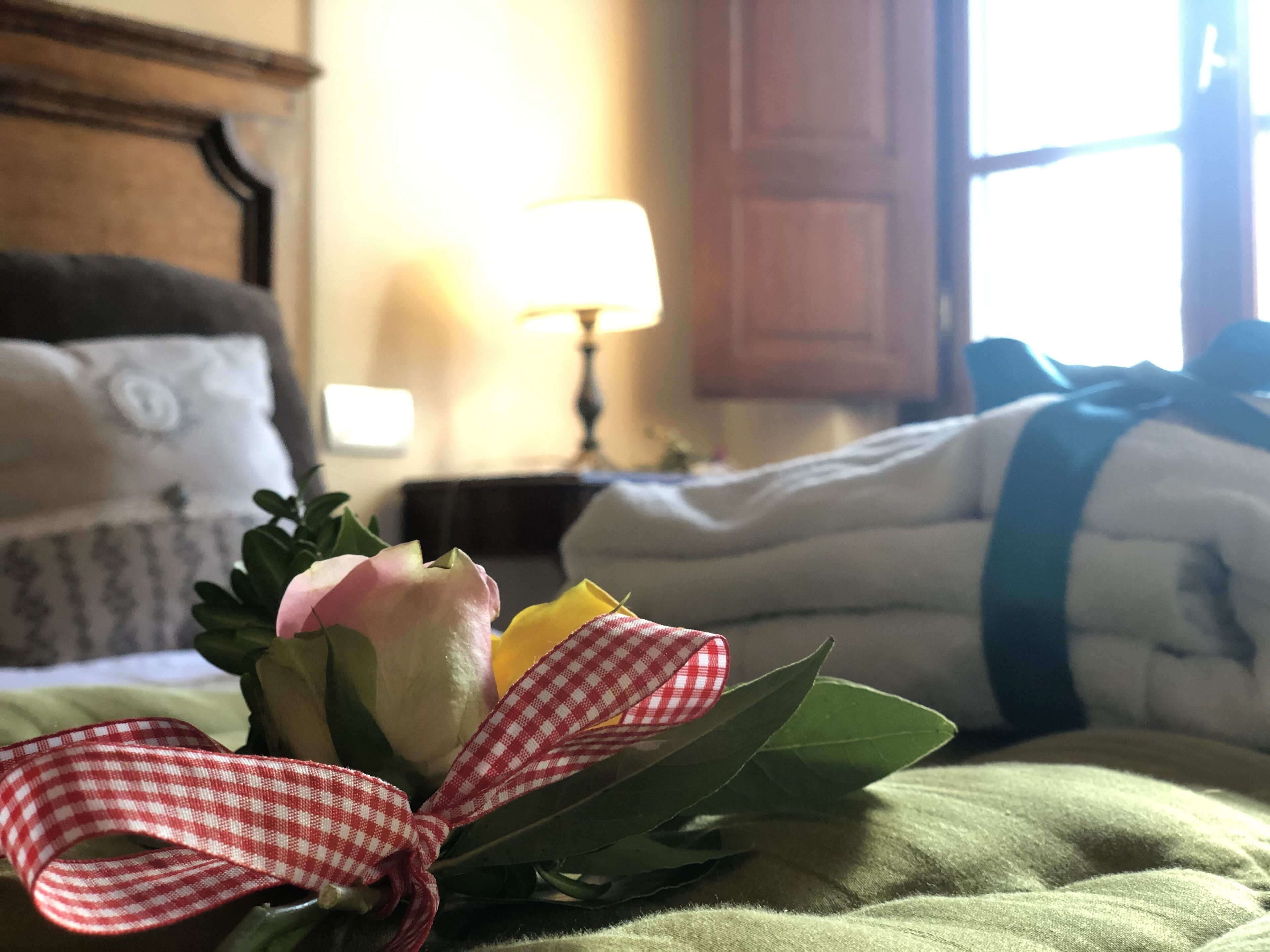 En säng med en bukett blommor och ett rutigt band, en lampa och ett fönster med gardiner.