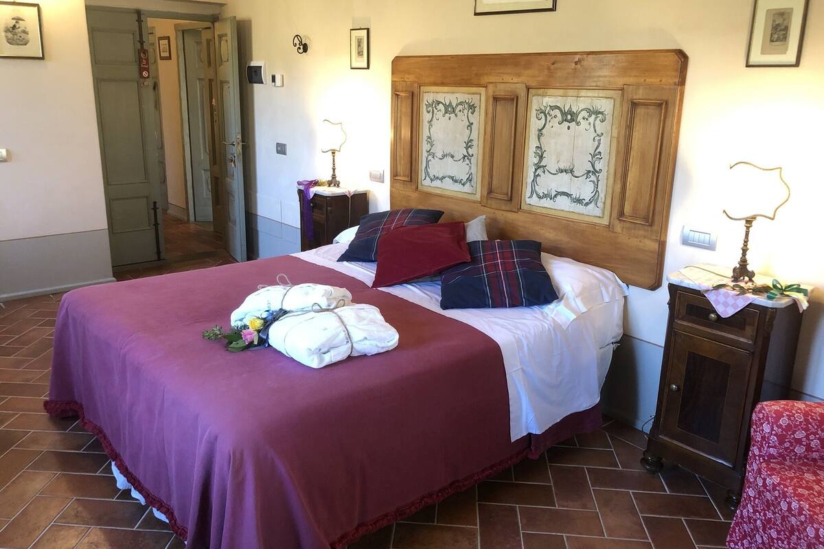 A hotel room with a large bed, a wooden headboard, a nightstand with a lamp, and a small table with a lamp.
