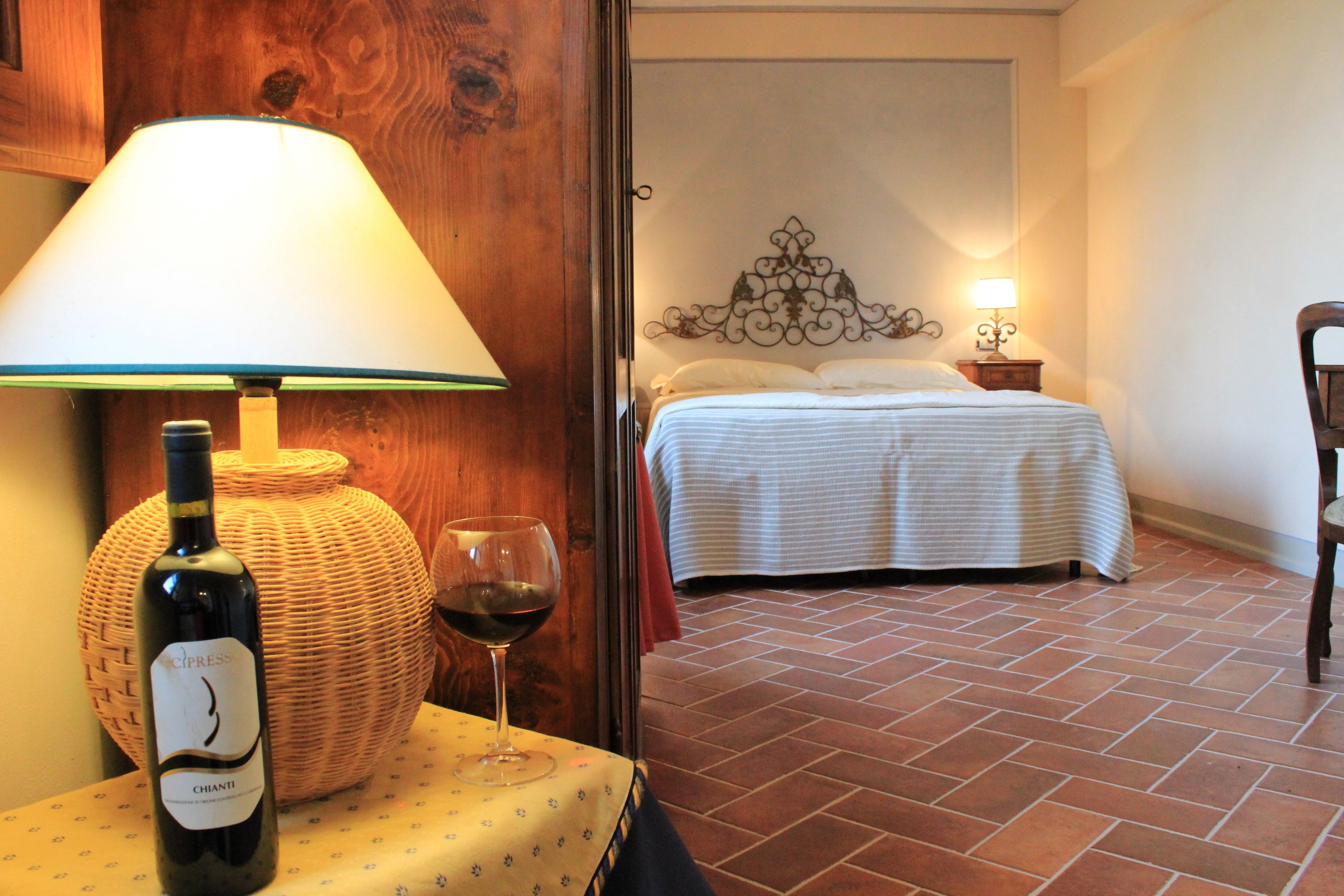 A room with a bed, a table with a bottle of wine, and a lamp.