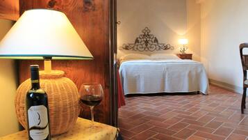 A room with a bed, a table with a bottle of wine, and a lamp.