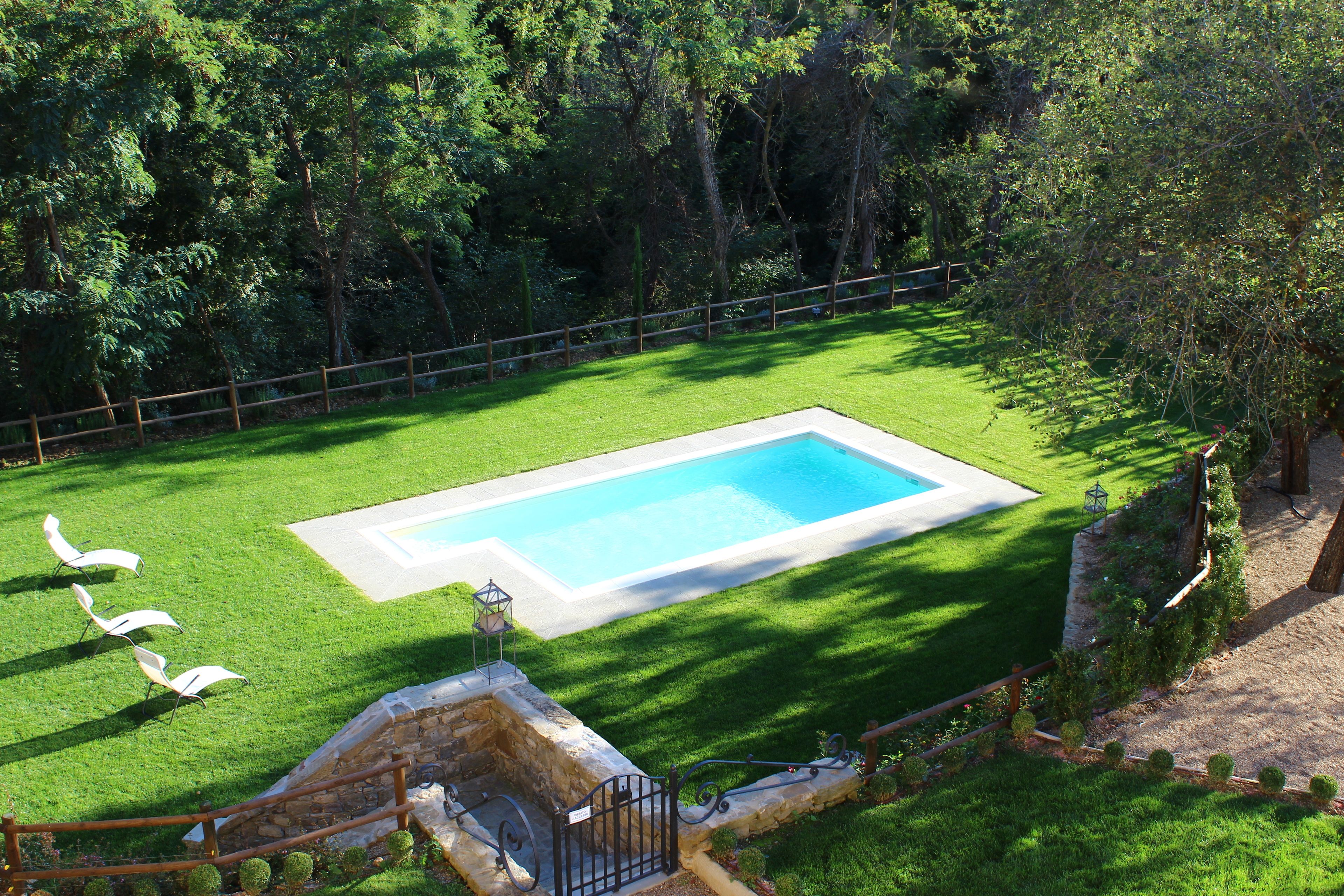 Piscina retangular com borda de pedra, cercada por um gramado bem cuidado e uma vedação de madeira.
