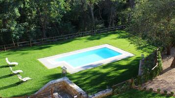 Piscina retangular com borda de pedra, cercada por um gramado bem cuidado e uma vedação de madeira.