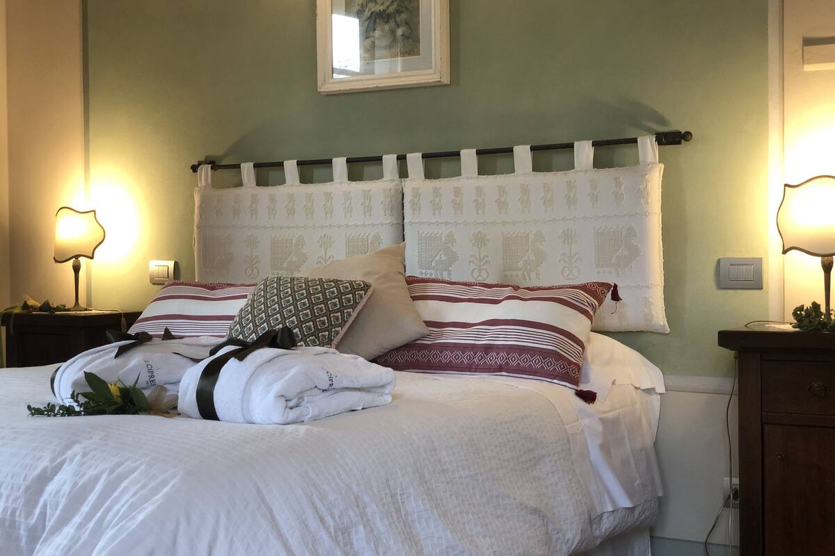 A neatly made bed with white linens and patterned pillows, a bedside lamp, and a framed artwork on the wall.