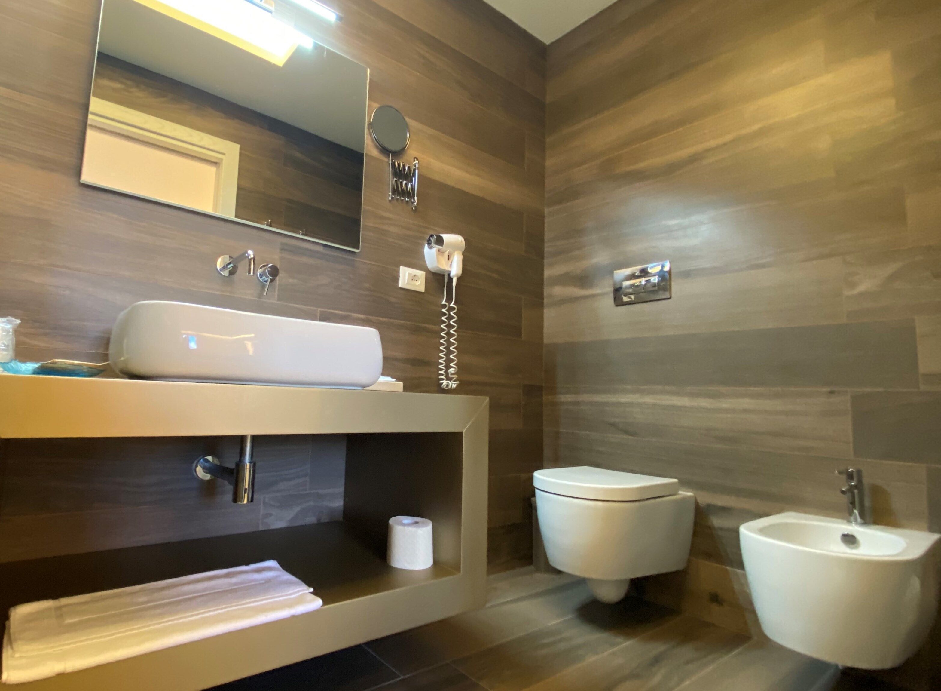 Ein modernes Badezimmer mit einem großen Spiegel, einem weißen Waschbecken, einem Bidet und einer Toilette.