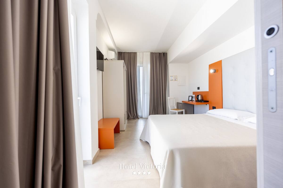 A hotel room with a bed, a desk, a chair, and a small table with a coffee machine.