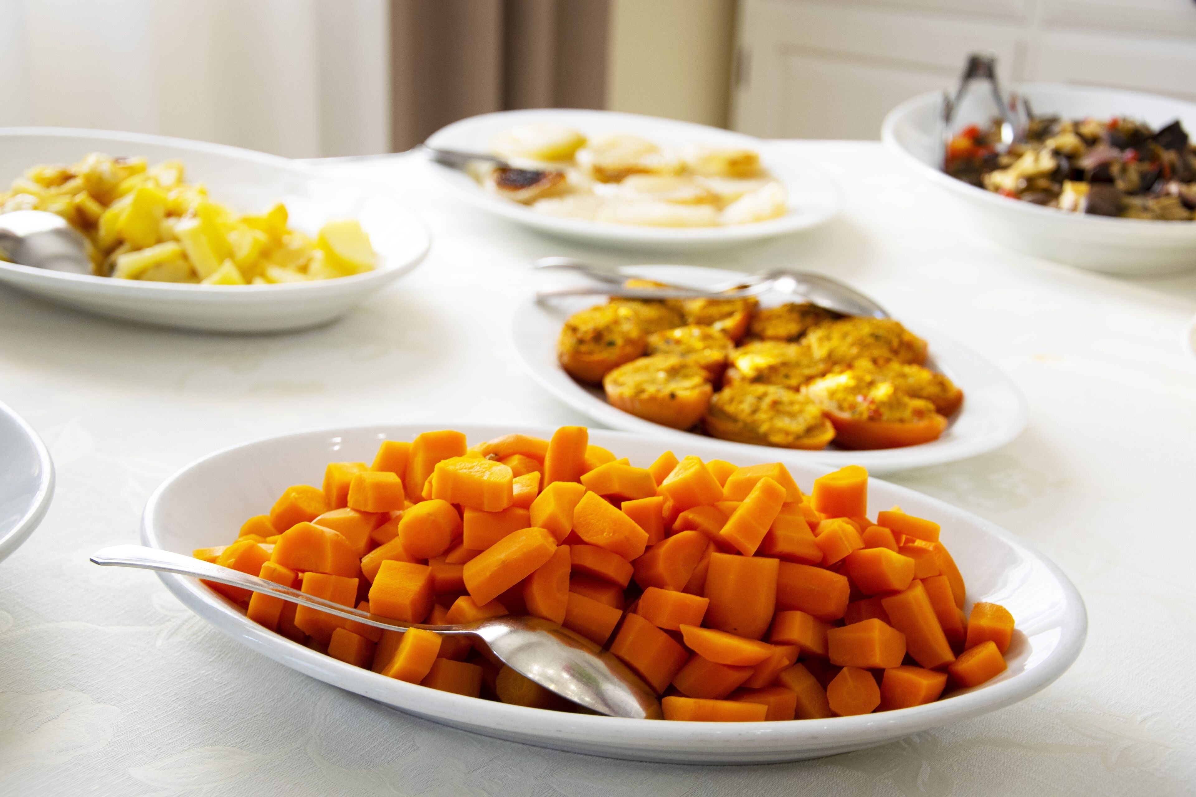 Une table où l’on trouve différents plats, notamment un bol de carottes coupées en dés, une assiette de pommes de terre en tranches et un plat de légumes rôtis.