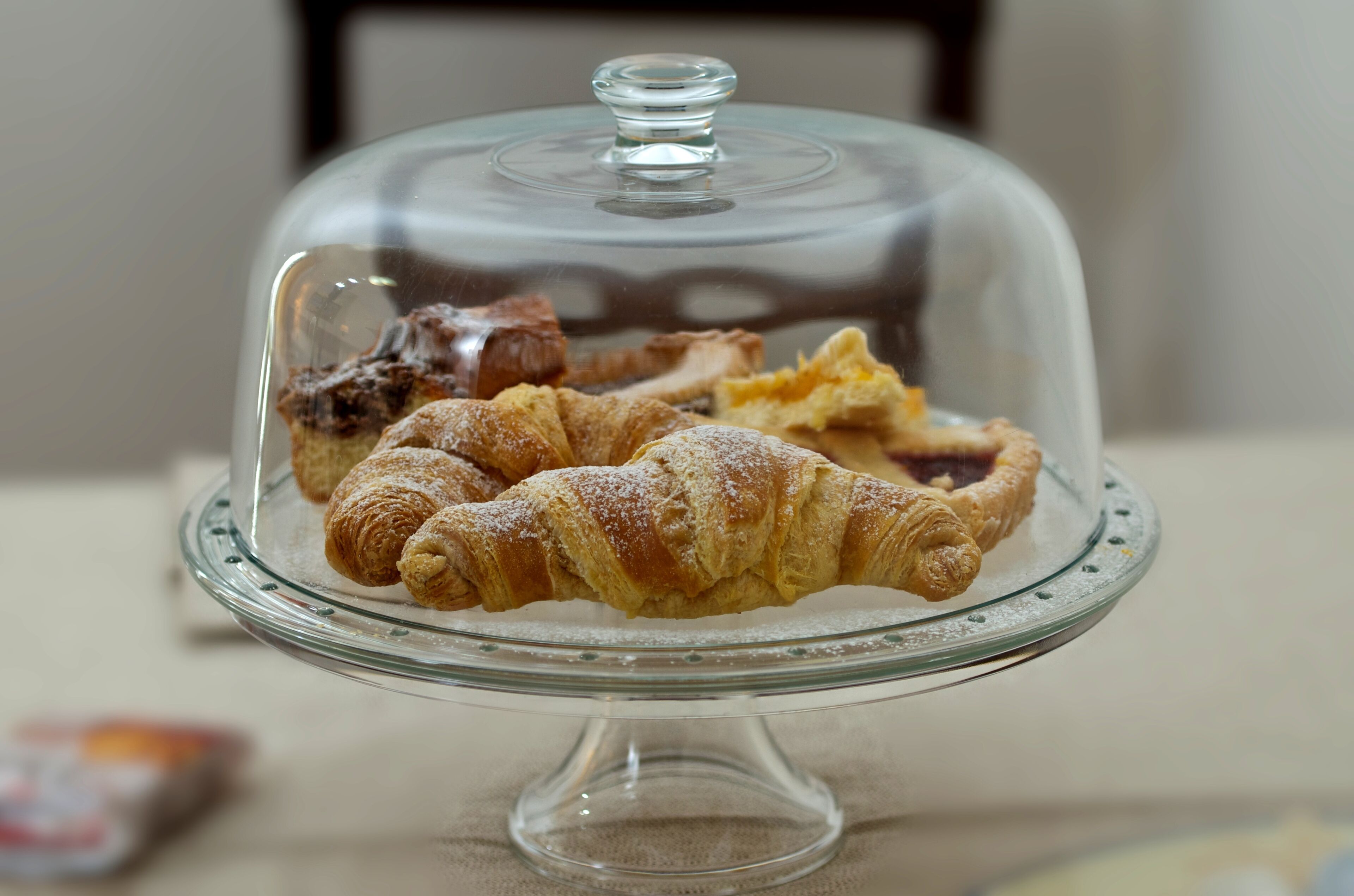A glass display case with a lid, containing several pastries including croissants and a pie.