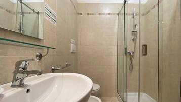Un baño con ducha de vidrio, lavamanos e inodoro.