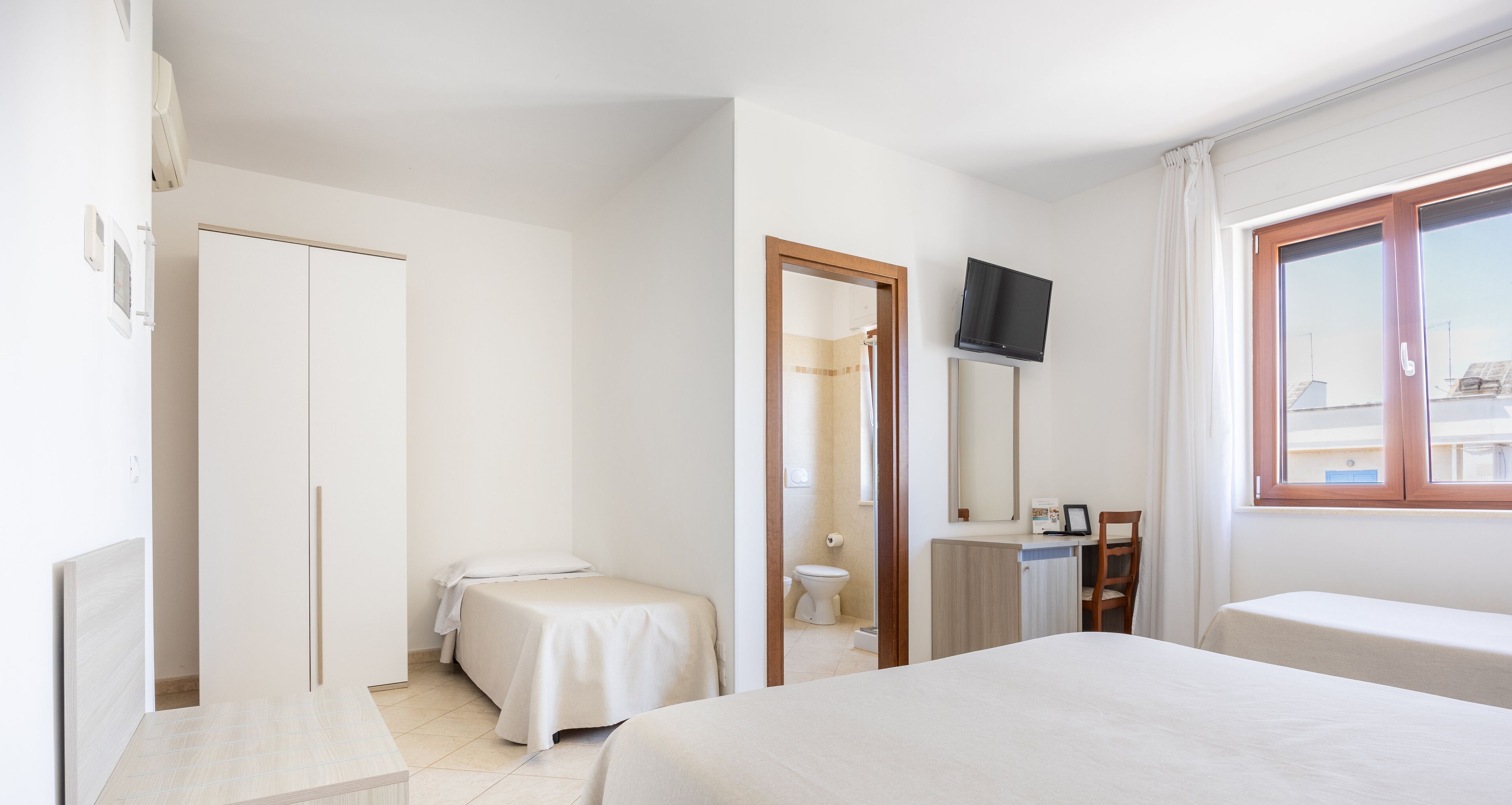A hotel room with a bed, a desk, a chair, a TV, and a window.