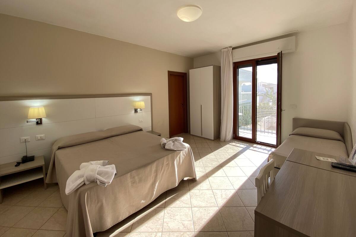 A hotel room with two beds, a desk, a wardrobe, and a balcony with a view.